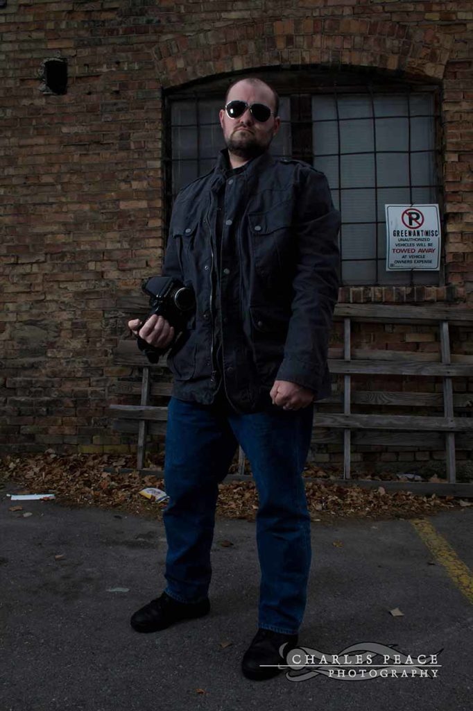 Photo. The photographer, standing in an alley, holding a camera.